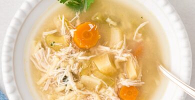 Chicken noodle soup served in a white bowl with fresh cilantro.