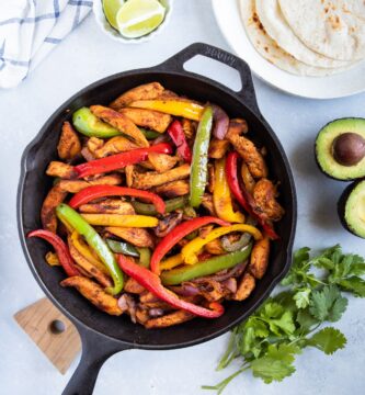 Fajitas de Pollo en un sartén con tortillas de harina, aguacate cilantro y rodajas de limon.