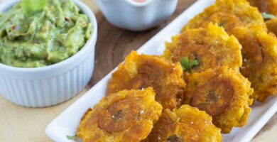 Tostones (Plátanos Verdes Fritos) servidos en un plato blanco con salsa de ketchup de mayonesa y guacamole en el costado.