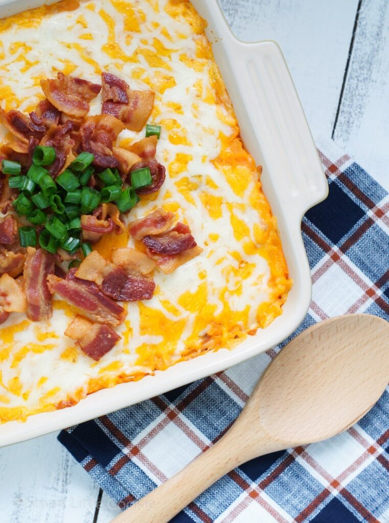 A loaded sweet potato casserole in a baking dish next to a wooden spoon.