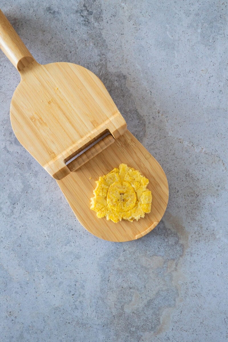 Después de la primera fritura, las rodajas de plátano se prensan suavemente para crear su forma clásica. Este paso es clave para lograr el equilibrio perfecto entre un exterior crujiente y un interior suave y tierno que hace que los tostones sean tan irresistibles.
