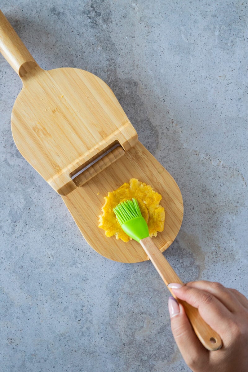 Después de la primera fritura, las rodajas de plátano se prensan suavemente para crear su forma clásica. Este paso es clave para lograr el equilibrio perfecto entre un exterior crujiente y un interior suave y tierno que hace que los tostones sean tan irresistibles.