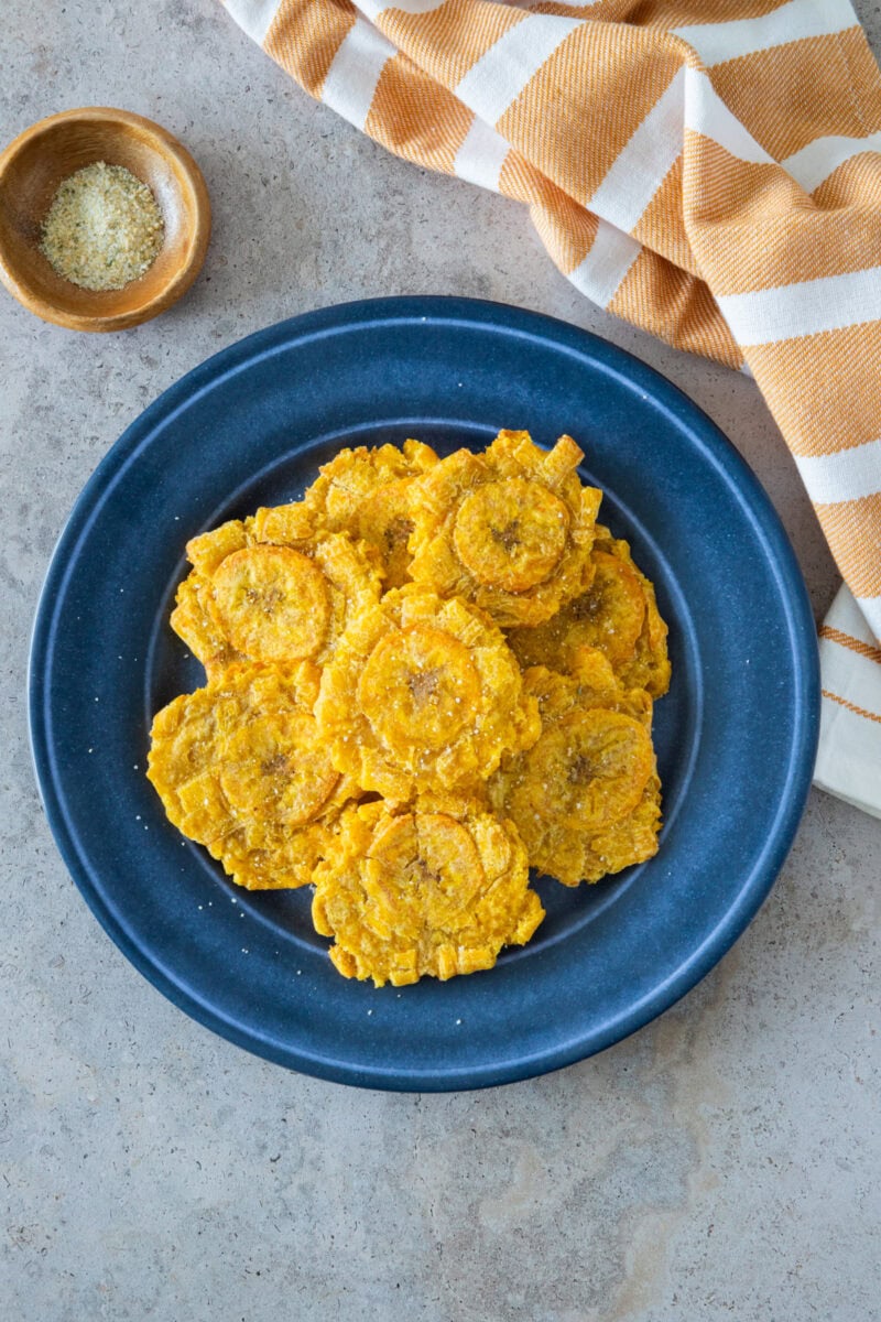 Tostones de freidora de aire servidos en un plato azul con sal marina.