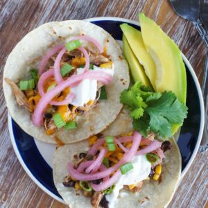 Two chicken chili tacos on a plate with sliced avocado.